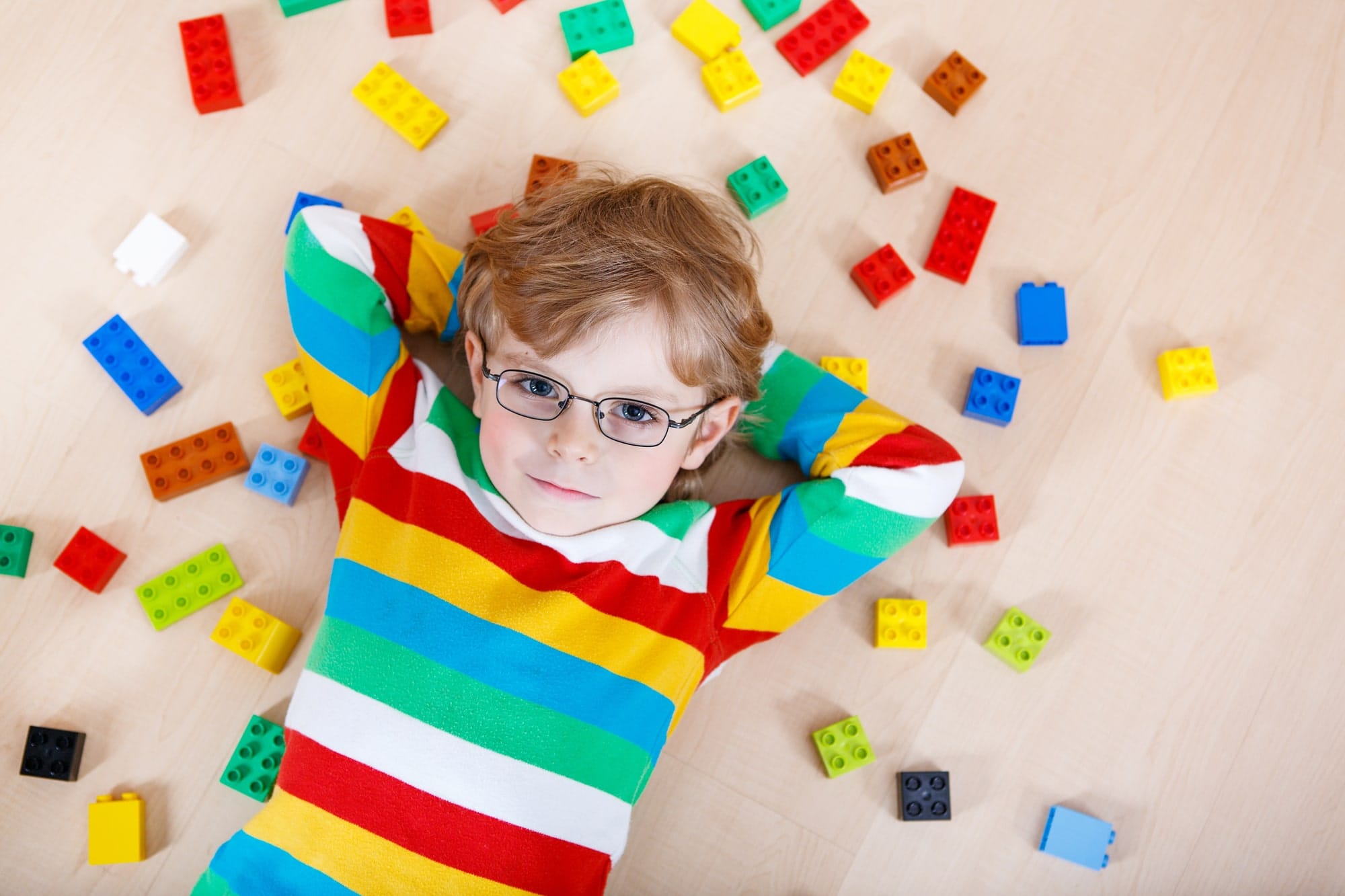 lego-swot-analysis-strengths Little blond kid boy playing with lots of colorful plastic blocks indoor. child wearing colorful shirt and glasses, having fun with building and creating.